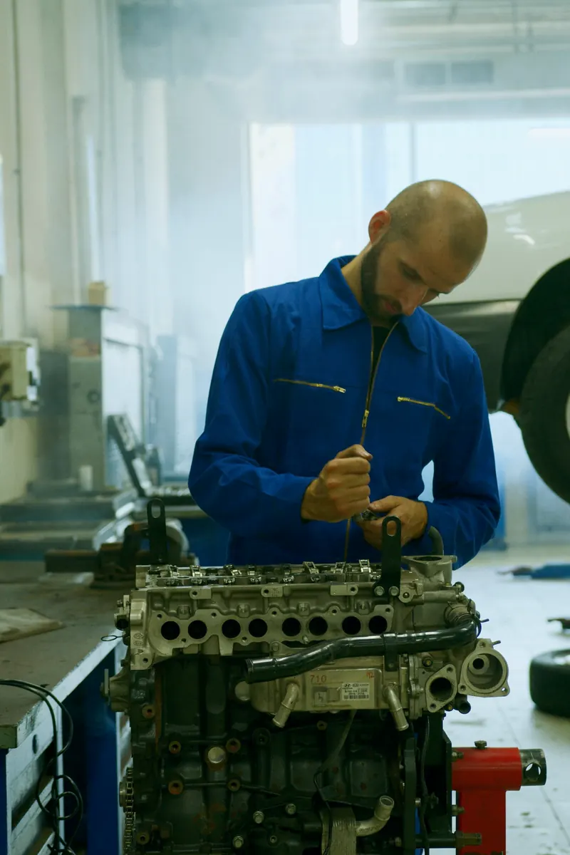 Mechanic in blue overalls working on an engine on a stand